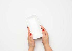 Female hands hold an empty rectangular disposable plastic container on a white background, top view photo