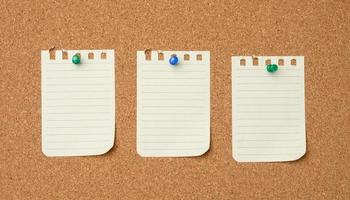 empty white sheet of paper attached with green buttons to a brown cork board photo