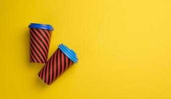 two paper red cups with a plastic lid on a yellow background, top view photo