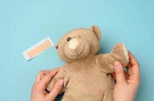 female hand holding a brown teddy bear with a torn off eye on a blue background photo