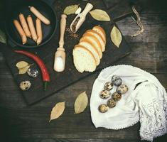 ausages in a black round cast-iron frying pan and raw quail eggs photo