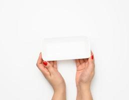 Female hands hold an empty rectangular disposable plastic container on a white background, top view photo