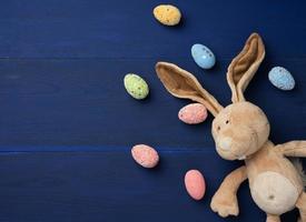 huevos de pascua decorativos y juguete de conejo de peluche suave con orejas largas sobre un fondo azul foto