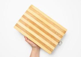 female hand with red manicure holds empty wooden rectangular kitchen chopping board on white background photo