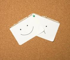 two paper leaves with a smile and a sad emotion attached with a button on a brown board photo