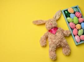 plush rabbit and decorative colorful Easter eggs in a wooden box on a yellow background photo