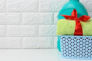 a rolled up terry green towel tied with a red silk ribbon and a plastic bottle of liquid laundry powder on a white shelf in the bathroom photo