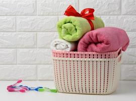 clean rolled terry towels in a plastic basket on a white shelf, bathroom interior photo