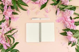 open spiral notebook with blank pages and a white pen on a peach background photo