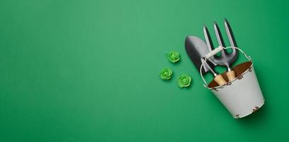 Miniature garden tools in a metal bucket on a green background, top view photo