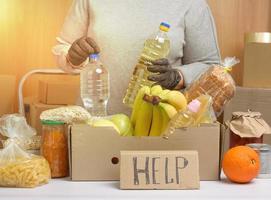 mujer en un suéter gris está empacando comida en una caja de cartón, el concepto de asistencia y voluntariado foto