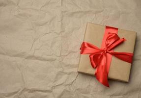 brown cardboard box tied with a silk red ribbon on a brown paper background photo