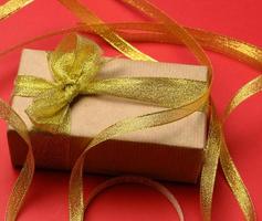 rectangular brown cardboard box tied with a silk ribbon on a red background photo