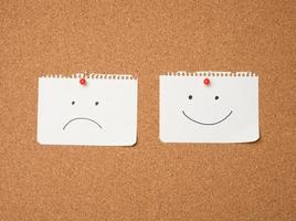 two paper leaves with a smile and a sad emotion attached with a button on a brown board photo