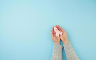 female hand holds a pink bow-shaped ribbon on a blue background photo