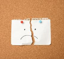 paper sheet with a sad emotion attached by a button on a brown board photo
