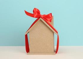 model of a wooden house tied with a red silk ribbon on a bluebackground, concept of real estate purchase photo