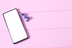 Mobile phone on pink table with headphones on table with cosmetics photo