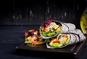 tortilla con tinta añadida envolturas de sepia con pollo y verduras sobre fondo negro. burrito de pollo, comida mexicana. foto