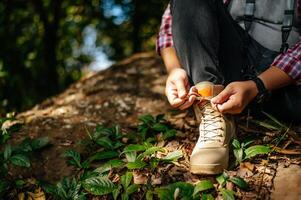 young man sitting and tying shoelaces during walking in trail photo