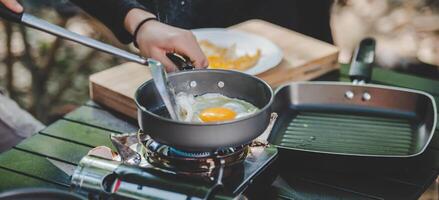 Young woman cooking with egg while camping with girl friend photo