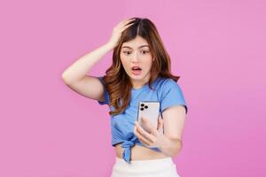 Portrait of frustrated young woman using mobile phone in her hands while standing isolated over pink background stressed with hand on head photo