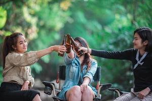 mujeres jóvenes sentadas y bebiendo bebidas mientras acampan en el bosque foto