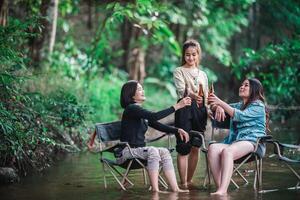 Young women sitting and drink beverage  while camping in forest photo