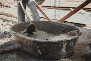 Worker man house builder mix mortar from a trough in bucket photo