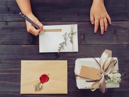 encima de la tarjeta de escritura de la chica de la mano y la caja de regalo artesanal en el fondo de la mesa de madera foto