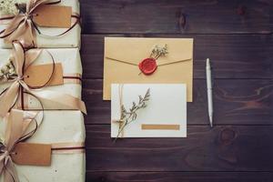 arriba de la caja de regalo artesanal y tarjeta de felicitación con bolígrafo sobre fondo de mesa de madera foto