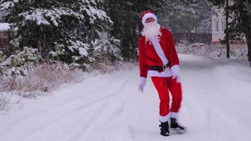 der weihnachtsmann hat spaß und lustiges tanzen, zeigt akrobatische tricks, kampfelemente und lustiges springen im winter im freien auf einer verschneiten straße mit kiefern. weihnachten und neujahr feiern. video