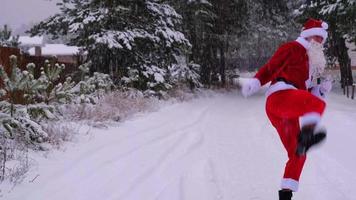 de kerstman claus is hebben pret en grappig dansen, shows acrobatisch trucs, elementen van vechten en grappig jumping buitenshuis in winter Aan een besneeuwd weg met pijnboom bomen. vieren Kerstmis en nieuw jaar. video