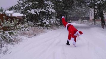 der weihnachtsmann hat spaß und lustiges tanzen, zeigt akrobatische tricks, kampfelemente und lustiges springen im winter im freien auf einer verschneiten straße mit kiefern. weihnachten und neujahr feiern. video
