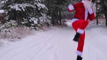 papai noel está se divertindo e dançando engraçado, mostra truques acrobáticos, elementos de luta e salto engraçado ao ar livre no inverno em uma estrada de neve com pinheiros. comemorando o natal e o ano novo. video