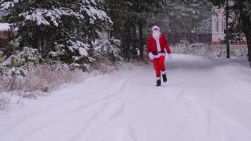 der weihnachtsmann hat spaß und lustiges tanzen, zeigt akrobatische tricks, kampfelemente und lustiges springen im winter im freien auf einer verschneiten straße mit kiefern. weihnachten und neujahr feiern. video