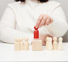 la mujer mantiene la figurilla de madera roja separada del grupo. concepto de crecimiento profesional, persona única. encontrar un empleado talentoso foto