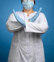 female medic in a white coat, a mask stands on a blue background, arms crossed photo