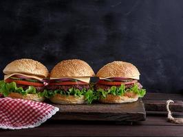 three hamburgers with vegetables on a brown wooden board photo