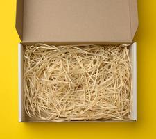 rectangular open corrugated paper box with sawdust inside. Packaging, containers for transportation on a yellow background photo