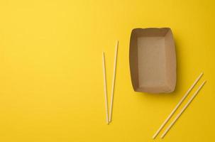 empty brown paper plate and wooden chopsticks on a yellow background, top view. Disposable tableware photo