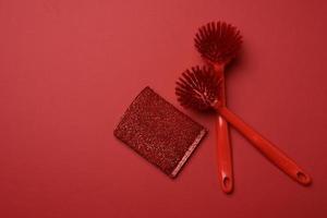 two red plastic brushes and a sponge for washing dishes on a red background photo