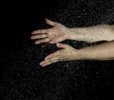 dos manos femeninas y gotas de agua voladoras sobre un fondo negro foto