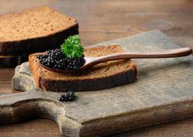 caviar de pez espátula negro granulado fresco en una cuchara de madera marrón sobre una mesa marrón foto