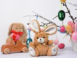 teddy bunny sitting on a white background and decorative colorful easter eggs hang on a branch photo