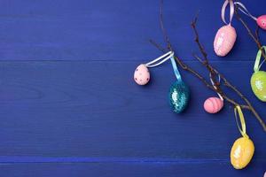 decorative easter eggs hang on a branch, blue wooden background photo