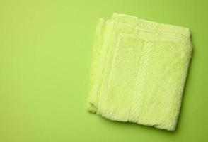 folded bath terry green towel on a green background, top view photo