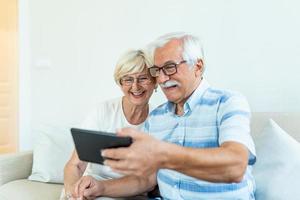 Senior couple using digital tablet at home. Grandparents using social media. Elderly couple together at home retirement concept using digital tablet photo