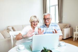 Senior couple is talking online via video connection on the laptop. Having nice time withfriends and family via video call waving on the camera photo