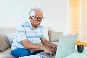 Mature businessman sit on sofa working on computer wireless device using e-banking application paying bills online, typing e-mail solve issues distantly, older generation and modern tech usage concept photo